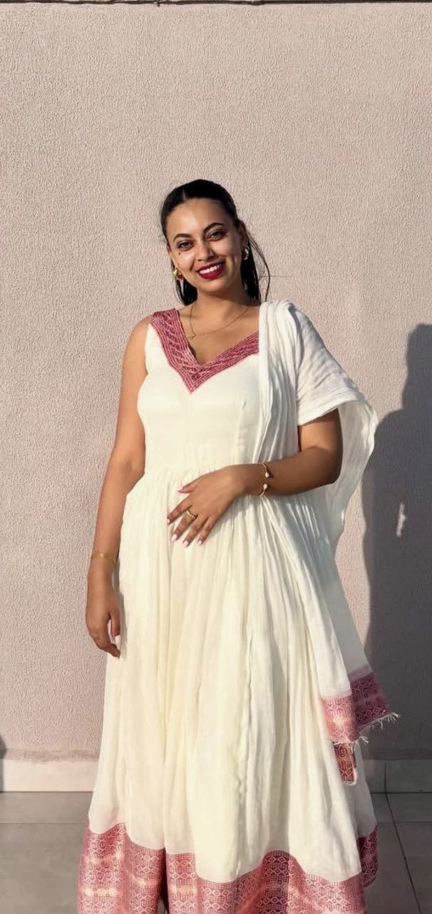 Sosi smiling outdoors in a white dress with pink embroidery
