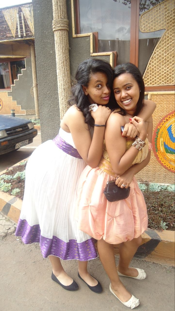 Sosi and a friend embracing outdoors, both dressed up in traditional Ethiopian dresses