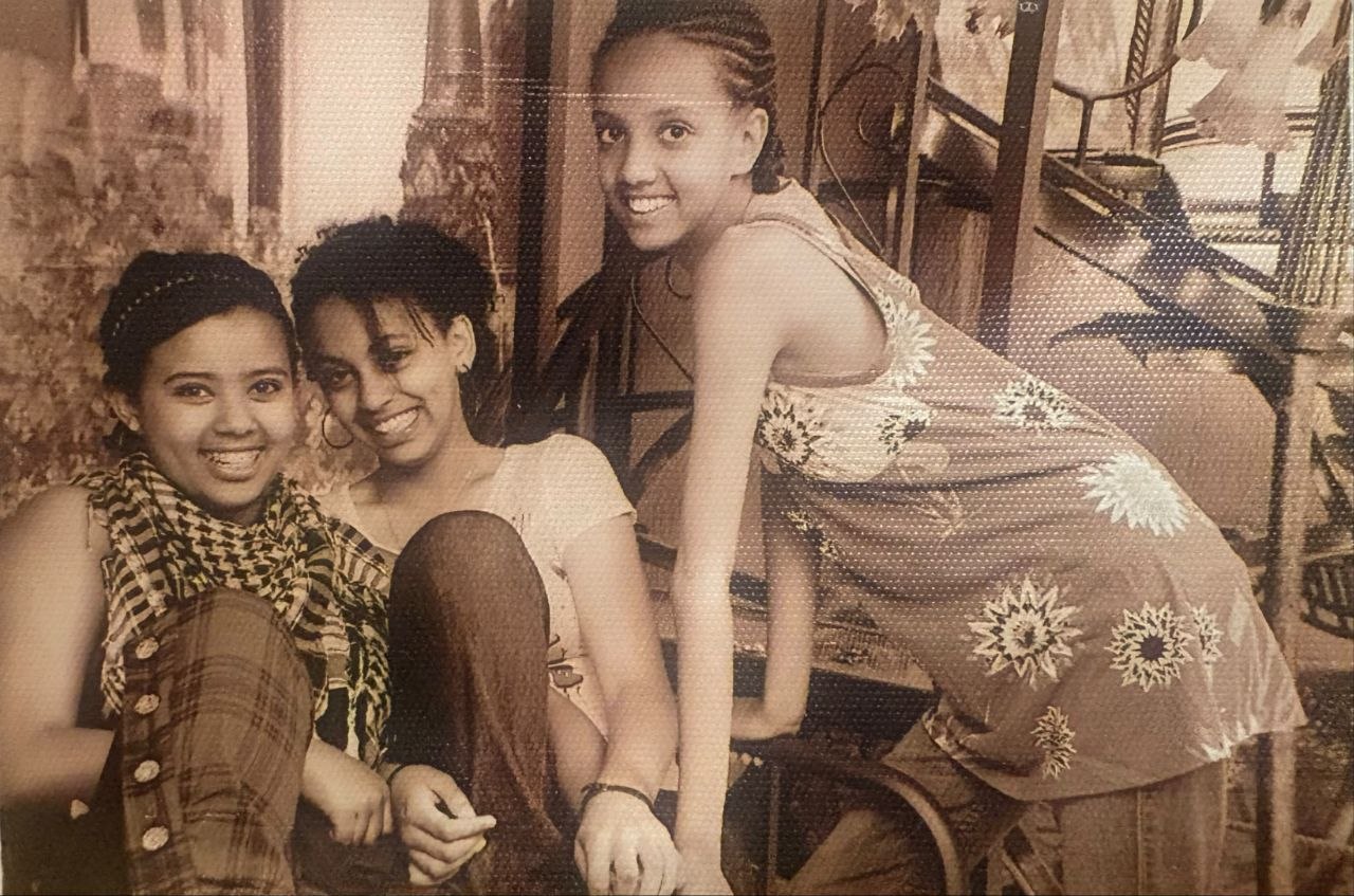 Faded studio photo of a young Sosi laughing with two friends against a vintage backdrop
