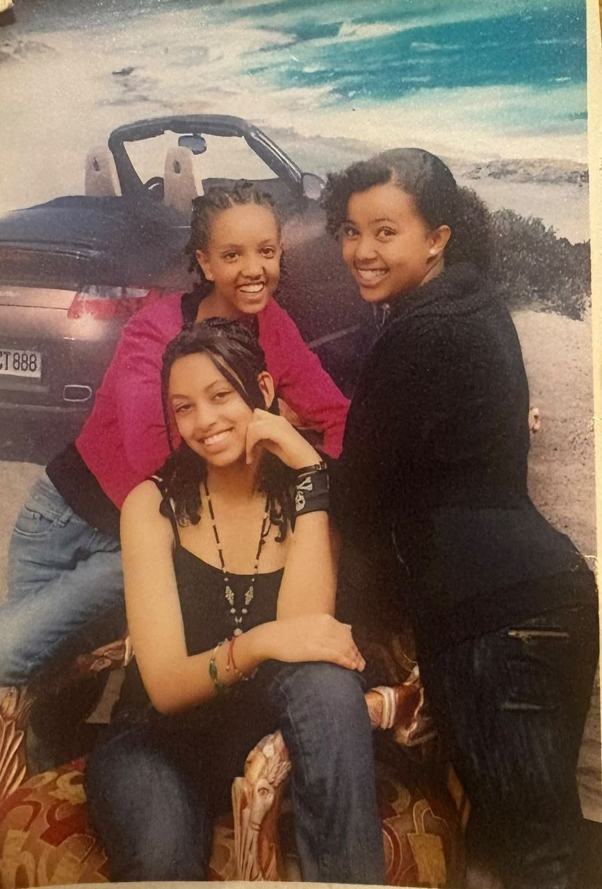 Sosi as a teenager posing with two friends against a painted car-and-beach studio backdrop